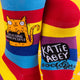 Detailed view of the “I F*cking Hate People” socks, featuring Katie Abey’s design. The vibrant rainbow stripes highlight an orange cat’s playful and unapologetic statement.