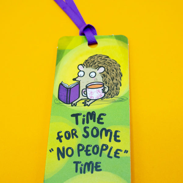 Katie Abey hedgehog bookmark close-up showing cute hedgehog reading a book and drinking tea with text “Time for some ‘No people’ time”. Bright green background with purple ribbon. Ideal quirky gift for readers, introverts and stationery lovers.