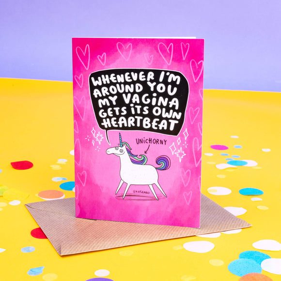 A sleazy looking white unicorn on a pink card with an arrow pointing to it saying 'UNIHORNY' Above that in a black speech bubble it says, 'Whenever I'm around you my vagina gets its own heartbeat.' It is on a pink card with hears and sparkles.