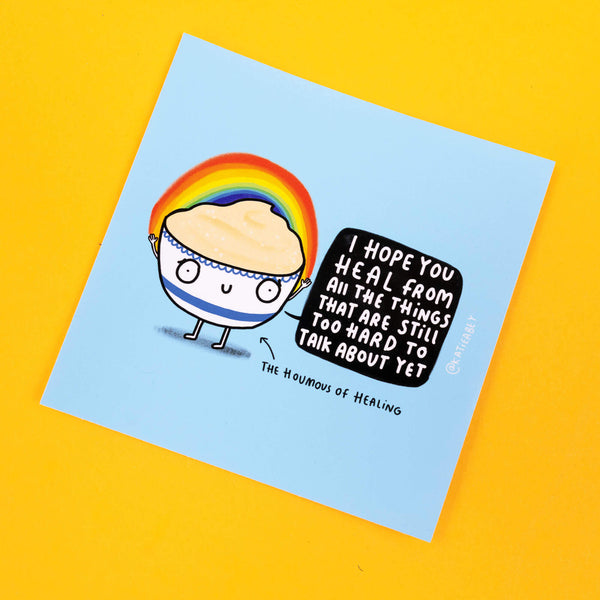 Katie Abey vinyl sticker featuring a cute, cartoon hummus character, with a rainbow arching above its head. The character holds a speech bubble that says, 'I Hope You Heal From All The Things That Are Still Too Hard To Talk About Yet', with the label 'The Houmous of Healing' beneath.