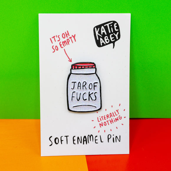 White jar shaped soft enamel pin with red lid and 'jar of f*ks' written on the front in black. The pin is attached with white cardboard with Katie Abey logo on top right hand side and red writing that says 'it's oh so empty' with an arrow to the far and 'literally nothing' with red dashes around the text under the jar. The pin is shown in front of rainbow coloured background.