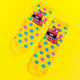 Yellow socks with blue and purple polka dots and pink cat illustration holding a black sign that reads 'go away'. The socks are laid out flat on a yellow background.