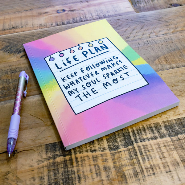 A notebook with a washed tie dye multicoloured vibe with an illustration by Katie Abey of a lined piece of paper on the front and Life Plan - Keep following whatever makes my soul sparkle the most on the front.