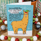 A playful blue Christmas card with a cartoon llama in a green elf hat. The card reads, "This is a heads up to let you know that the Christmas Llama will be watching you over the festive period to make sure you wholeheartedly enjoy yourself (no pressure)." Festive baubles and holiday decor are placed around the card.