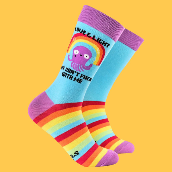 Colourful crew socks by Katie Abey featuring a purple octopus, a rainbow, and the phrase "Love & Light But Don't F**k With Me." These fun and quirky socks showcase rainbow stripes and purple accents, embodying the brand's playful weirdness and bold self-expression.