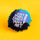 Close-up of a Katie Abey “Don’t Make Sense Make Art” enamel pin badge with a rainbow metal finish and white handwritten style text, set against a bright yellow background. The scalloped edge pin features a pencil illustration, highlighting a bold, creative and alternative aesthetic.