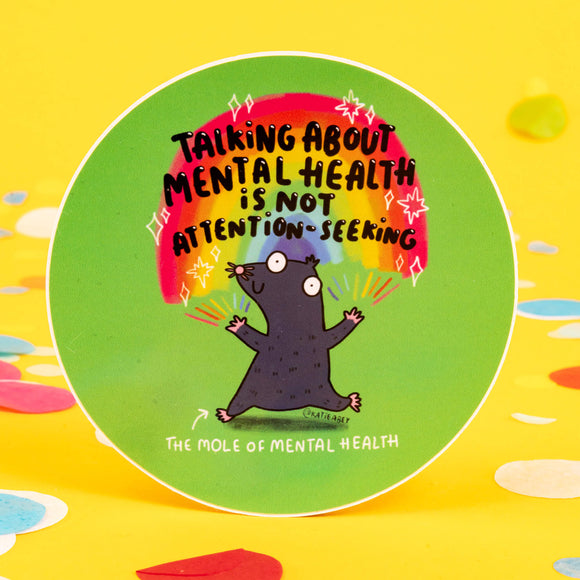 Green circular sticker of a mole with rainbows coming from its fingertips with text above saying talking about mental health is not attention seeking 