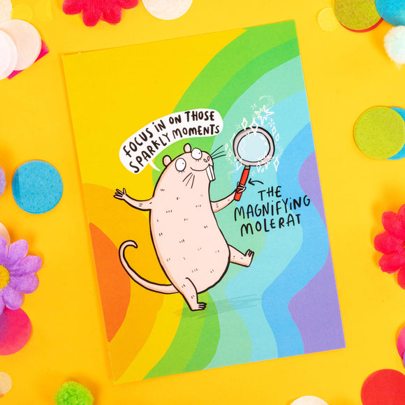Fun cute A6 silk finish greeting postcard, featuring illustrated happy molerat holding magnifying glass, on colourful rainbow background. Reading 'The magnifying molerat' and 'focus in on those sparkly moments' in black letters and speech bubble. Designed by Katie Abey in the UK.