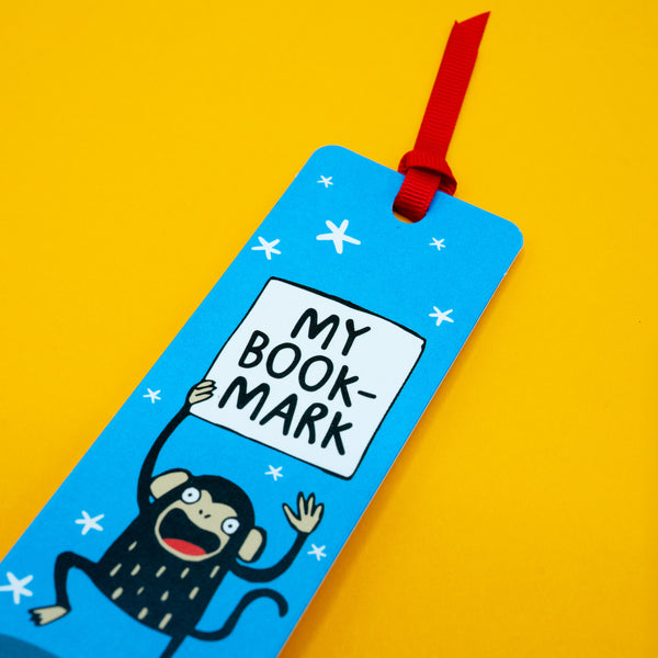 Close-up of Katie Abey My Bookmark Monkey bookmark featuring a cute cartoon monkey holding a sign that reads “My Bookmark”. Blue background with white stars and red ribbon. Fun, quirky reading accessory gift.
