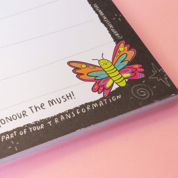 Close-up of a colourful butterfly illustration on a notepad by Katie Abey, featuring the text “Honour The Mush!” on a pastel pink background. Perfect for adding a magical touch to your notes and reflections.