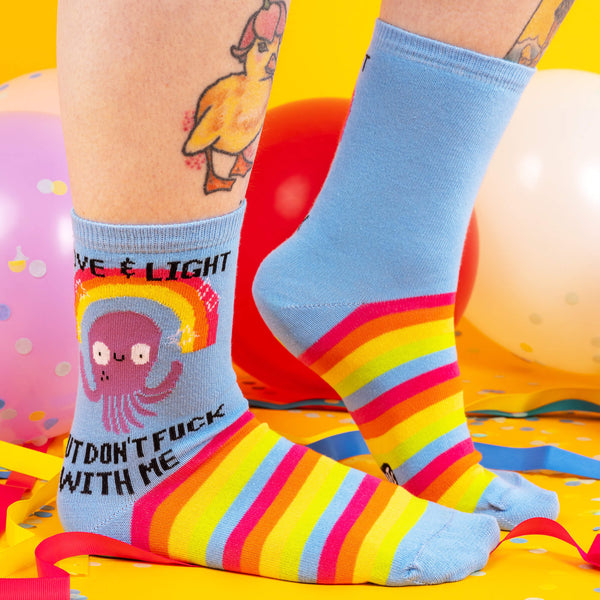 a pair of socks on some feet which are blue with rainbows with an octopus on with text saying love and light but don't fuck with me