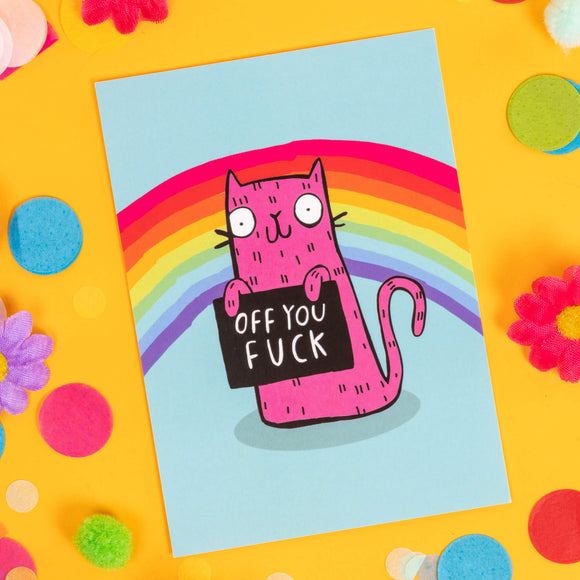 A6 greetings postcard featuring a funny sweary smiley pink cat holding a black sign which reads 'Off you...', on a blue background with a rainbow. Designed by Katie Abey in the UK