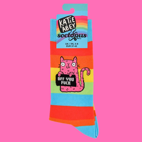 Close-up of Katie Abey rainbow striped socks, featuring a cheeky pink cat holding a sign with "Off You F***". Packaging highlights the brand's playful, bold design. Quirky, colourful socks for those who love adding a touch of humour to their wardrobe.