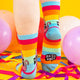 back of a model with tattooed legs wearing Katie Abey off you fuck socks with pink cat holding a sign. They are rainbow striped and lovely and vibrant. The model is stood on a yellow floor with balloons, confetti and ribbons