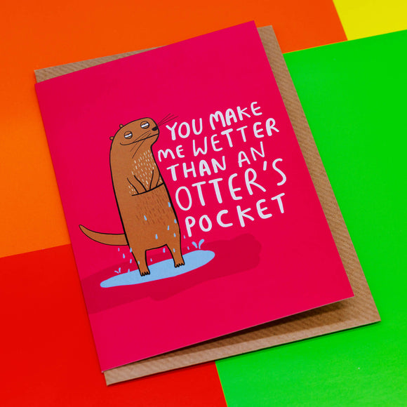 A cheeky looking illustrated otter by Katie Abey with their hand in their pocket standing in a puddle with text next to it saying 'you make me wetter than an otters pocket against a primary colour background
