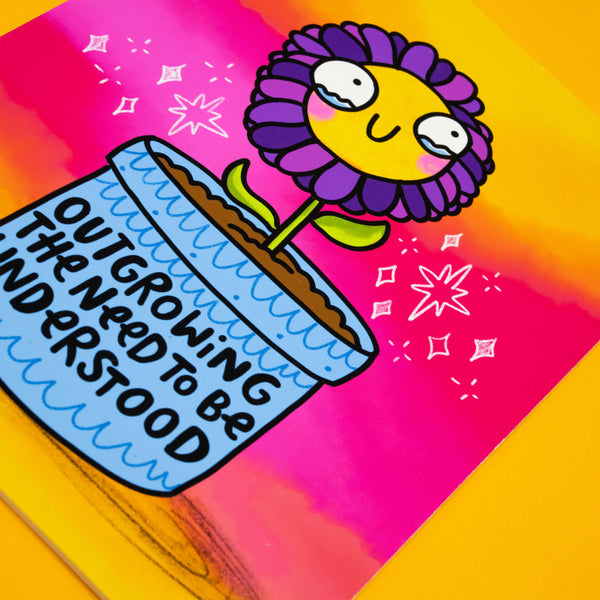 Close-up of Katie Abey’s Outgrowing The Need To Be Understood flower art print. Features a cute purple flower with a smiling yellow face in a blue plant pot against a bold pink and orange background. Quirky wall art illustration, A4 size, matte finish, limited edition print.