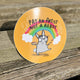 A sticker on wooden decking with a drawing by Katie Abey of a rabbit with a paint brush and a rainbow behind it with text saying pay an artist not a robot