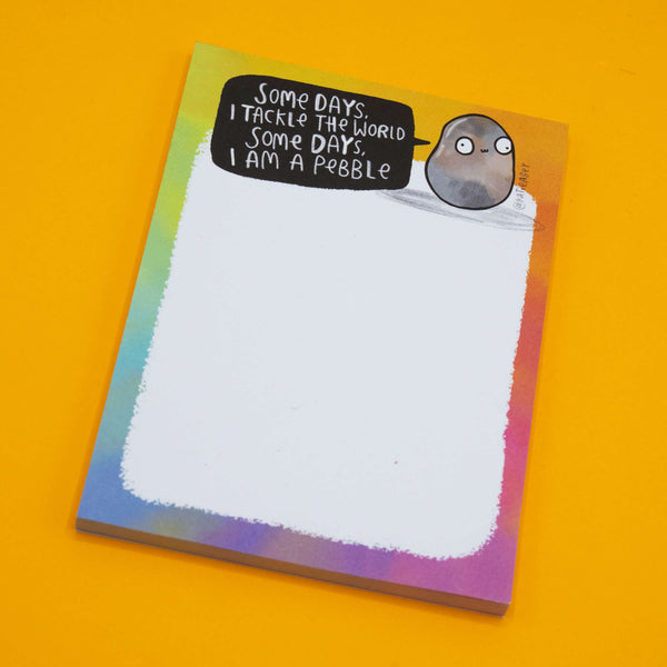 Angled shot of the Katie Abey "Some Days I Am A Pebble Pad" rainbow stationery notepad featuring a funny pebble character illustration. Cute and motivational desk pad from small UK illustrator brand Katie Abey.