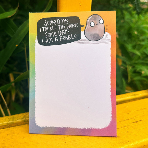 Katie Abey "Some Days I Am A Pebble" A6 notepad with a rainbow border and quirky pebble illustration. The pad features the quote “Some days, I tackle the world. Some days, I am a pebble” with 50 tear-off pages for fresh lists. Perfect pocket-sized stationery from illustrator Katie Abey, encouraging you to embrace your weirdness.