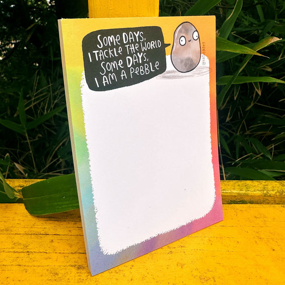 "Some Days I Am A Pebble" notepad by Katie Abey, featuring a cute pebble character and motivational quote. A6 pad with rainbow edges and 50 easy-tear pages, ideal for jotting lists, notes, or doodles. Fun, pocket-sized stationery gift from Katie Abey, a small business known for colourful, quirky designs.