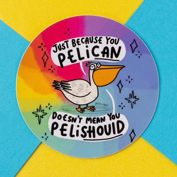 A circular sticker designed by Katie Abey featuring a quirky cartoon pelican on a colourful rainbow background. The text reads, "Just because you PELICAN doesn’t mean you PELISHOULD." The design encourages playful wordplay and embracing your weirdness, consistent with Katie Abey's unique, whimsical style.