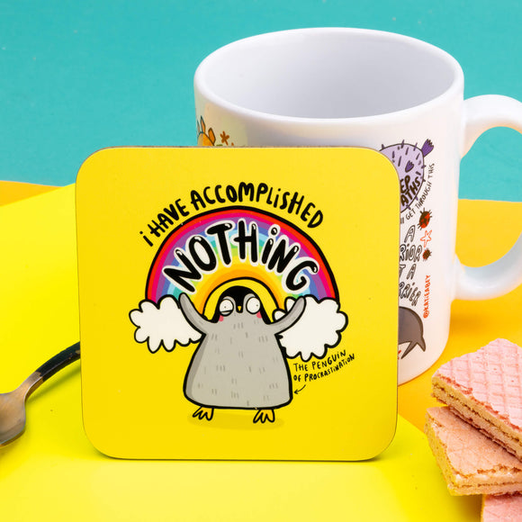 The Penguin of Procrastination Coaster. The coaster is a yellow background with a baby penguin holding its arms up with a rainbow and text behind it reading 'I have accomplished NOTHING'. There's an arrow pointing at the bottom of the penguin with text reading 'the penguin of procrastination'. Designed by Katie Abey in the UK.