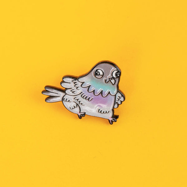 A whimsical enamel pin by Katie Abey featuring a cute pigeon with a pastel iridescent shimmer and expressive eyes. The pigeon is perched against a bright yellow background, highlighting its quirky design. A perfect gift for animal pin collectors or weird art fans.