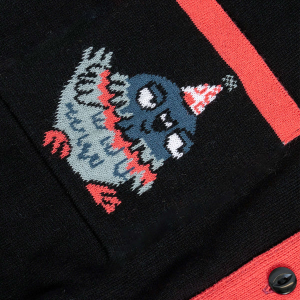 Close up of pigeon graphic on pocket of the Katie Abey x Rebel Romance Pigeon Party Long Cardigan. Cute wide eyed pigeon wearing a party hat on black knit with red trim detail. Soft alternative long cardigan by Katie Abey.
