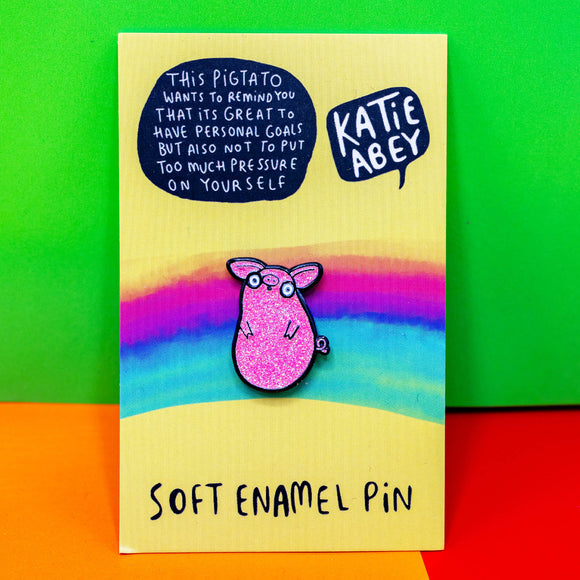 a sparkly pink pig pin with round eyes on its backing card with text reading 'this pigtato wants to remind you that its great to have personal goals but also not to put too much pressure on yourself. Designed by Katie Abey in the UK