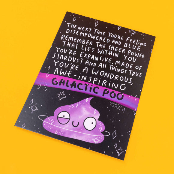 Colourful postcard by Katie Abey with a motivational message in white text on a black background: "The next time you're feeling disempowered and blue, remember the sheer power that lies within you. You're expansive, made of stardust and all things true. You're a wondrous, awe-inspiring galactic poo." The bottom features a cute, purple cartoon poo with a smiling face, set against a galaxy backdrop. The artist's handle, @katieabey, is visible. The background is bright yellow