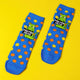 Blue socks on yellow background with fluffy rainbow balls sprinkled around. The blue socks have orange and yellow polka dots. Socks have lime greet cat illustration holding a black sign with 'poo poo head' written on in white letters.