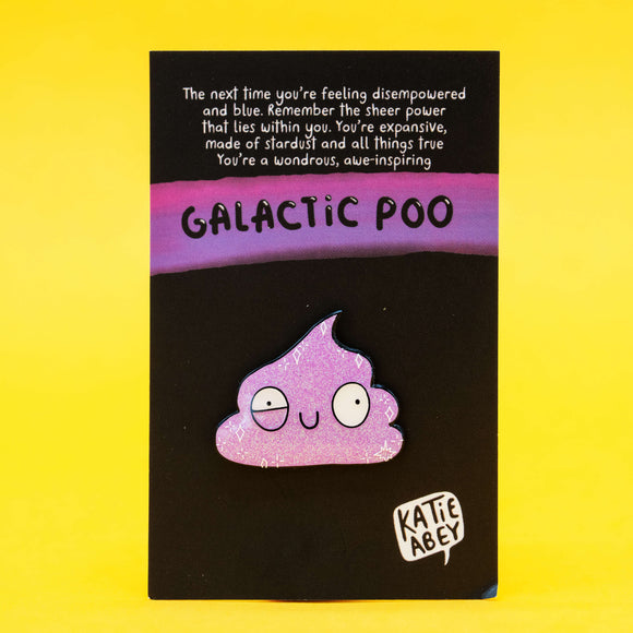 Close-up of the Galactic Poo enamel pin on its backing card by Katie Abey. The sparkly purple poo character has big cartoon eyes, black outlines, and sits under an empowering stardust-themed quote.