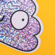 A glittery purple poop-shaped sticker with a funny expression, featuring googly eyes and a lopsided smile. The background is bright yellow. This playful design is from Katie Abey, a small colourful company for fun likeminded weirdos.