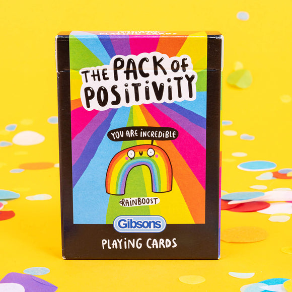 A pack of playing cards with a rainbow smiling on the front illustrated by Katie Abey. It is on a yellow background with confetti 