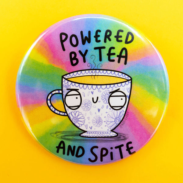 Round badge with a rainbow tie-dye background featuring a mischievous looking floral teacup illustration and the phrase “Powered by Tea and Spite” in bold black lettering. Set against a bright yellow backdrop.