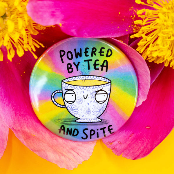 Badge with the phrase “Powered by Tea and Spite” nestled in bright pink and yellow flower petals. The illustrated floral teacup character looks unimpressed on a rainbow tie-dye background.