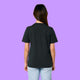 Back view of a black Katie Abey Prioritising Whimsy, Nonsense and Joy adults graphic t-shirt worn by a model against a purple background. The organic cotton unisex tee shows a relaxed everyday fit with a plain back and short sleeves.
