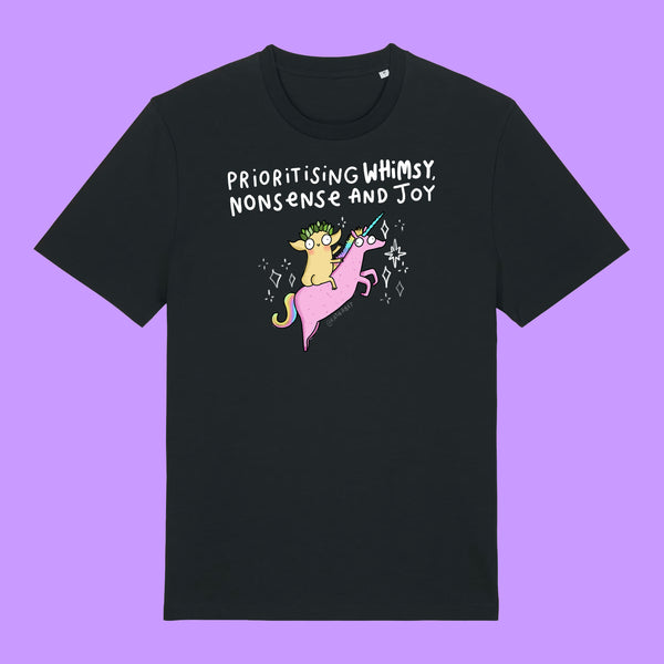 Front view of a black Katie Abey Prioritising Whimsy, Nonsense and Joy adults graphic t-shirt featuring a colourful unicorn illustration and playful text. Whimsical organic cotton tee photographed on a purple background.