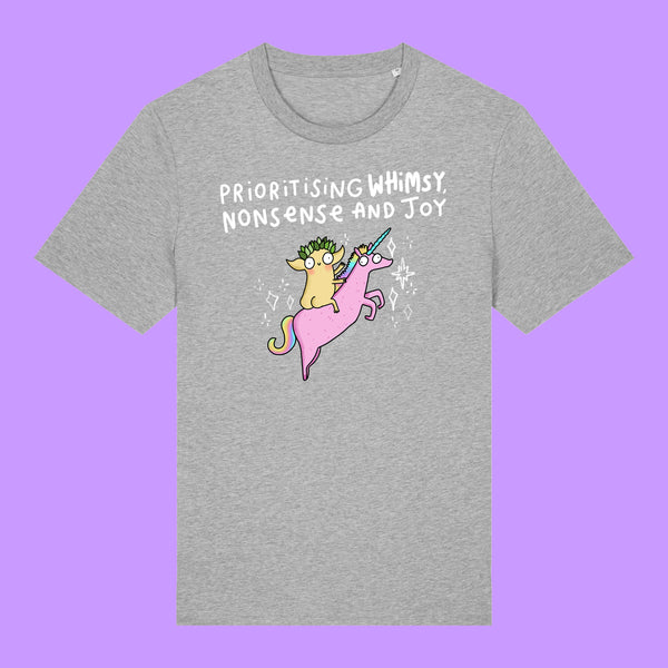 Front view of a heather grey Katie Abey Prioritising Whimsy, Nonsense and Joy adults graphic t-shirt. Features a colourful illustration of a quirky character riding a pink unicorn with playful lettering above, photographed on a purple background.
