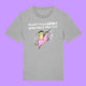 Front view of a heather grey Katie Abey Prioritising Whimsy, Nonsense and Joy adults graphic t-shirt. Features a colourful illustration of a quirky character riding a pink unicorn with playful lettering above, photographed on a purple background.