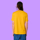 Back view of a Spectra Yellow Katie Abey Prioritising Whimsy, Nonsense and Joy adults t-shirt worn by a model with dreadlocks. The organic cotton unisex tee shows a relaxed fit and plain back against a purple background.