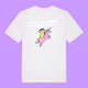 Front view of a white Katie Abey Prioritising Whimsy, Nonsense and Joy adults graphic t-shirt featuring a colourful unicorn illustration and playful text. Whimsical organic cotton tee photographed on a purple background.
