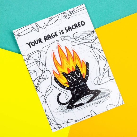A postcard of a black cat on fire on a white background with back squiggles it has text above saying Your rage is sacred. Illustrated by Katie Abey