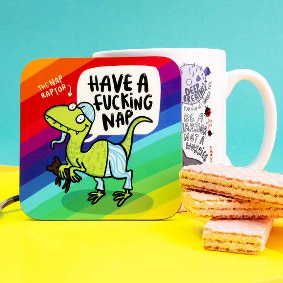 The coaster is a rounded corner square shape with a rainbow stripe background and a green raptor dinosaur smiling wearing pyjamas and holding a teddy bear. There's some text that read the 'The Nap Raptor' with an arrow pointing at the dinosaur and a speech bubble reading 'Have a fucking nap'.