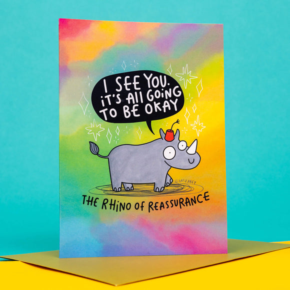 funny A6 greeting card featuring The Rhino of Reassurance designed by Katie Abey. The Rhino is wearing a red hat with a speech bubble coming from it's mouth that reads 'I see you it's all going to be okay'. The card is multicoloured with a gold envelope.