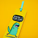 Reading is Roar Some Dinosaur Bookmark by Katie Abey showing cute green cartoon dinosaur with speech bubble text, bright yellow background and turquoise ribbon, playful illustrated bookmark by UK small business celebrating reading and creativity.