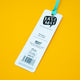 Back of Reading is Roar Some Dinosaur Bookmark by Katie Abey, featuring white card with branding, barcode and recycling details, attached to a turquoise ribbon, photographed on a bright yellow background, fun illustrated bookmark by quirky UK artist.