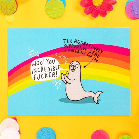 A postcard with a clapping seal saying Woo! You incredible fucker!"  There is an arrow with text above it The aggressively supportive seal is cheering for you. The background of the postcard is blue with a rainbow going through it.
