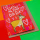 A red card with a dik dik with red hearts behind it saying show me your Dik-Dik. It is sat on its envelope on a primary coloured background.