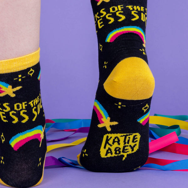 A white model with tattooed legs wearing black socks with yellow heels and band around the top with shooting stars and writing saying the socks of success designed by Katie Abey